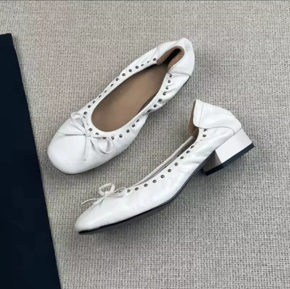 Ballerine bianche con fiocchetto e borchie, vista laterale di un paio accostato