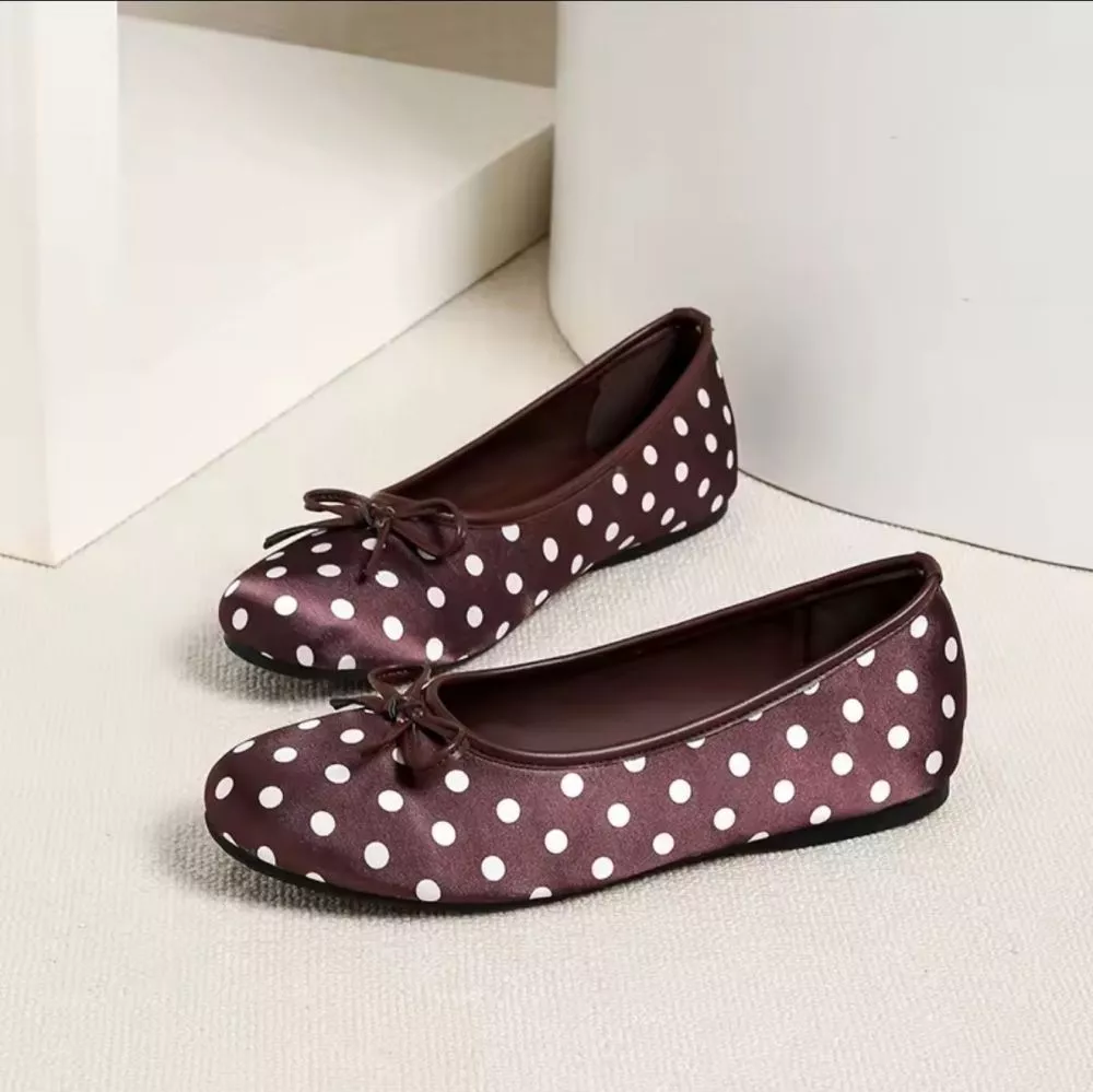 Ballerine donna marrone con pois bianchi e fiocco, viste lateralmente, su pavimento chiaro.