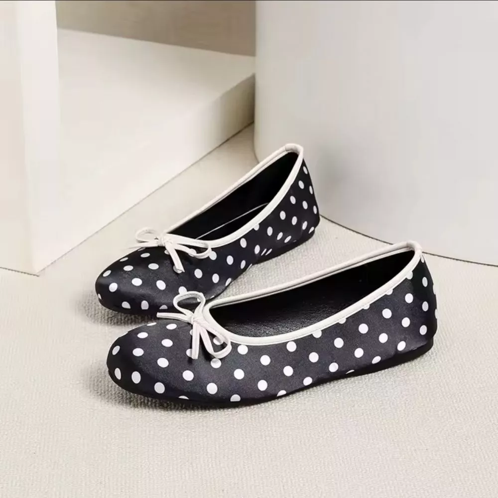 Ballerine donna nero con pois bianchi e fiocco, viste lateralmente, su pavimento chiaro.