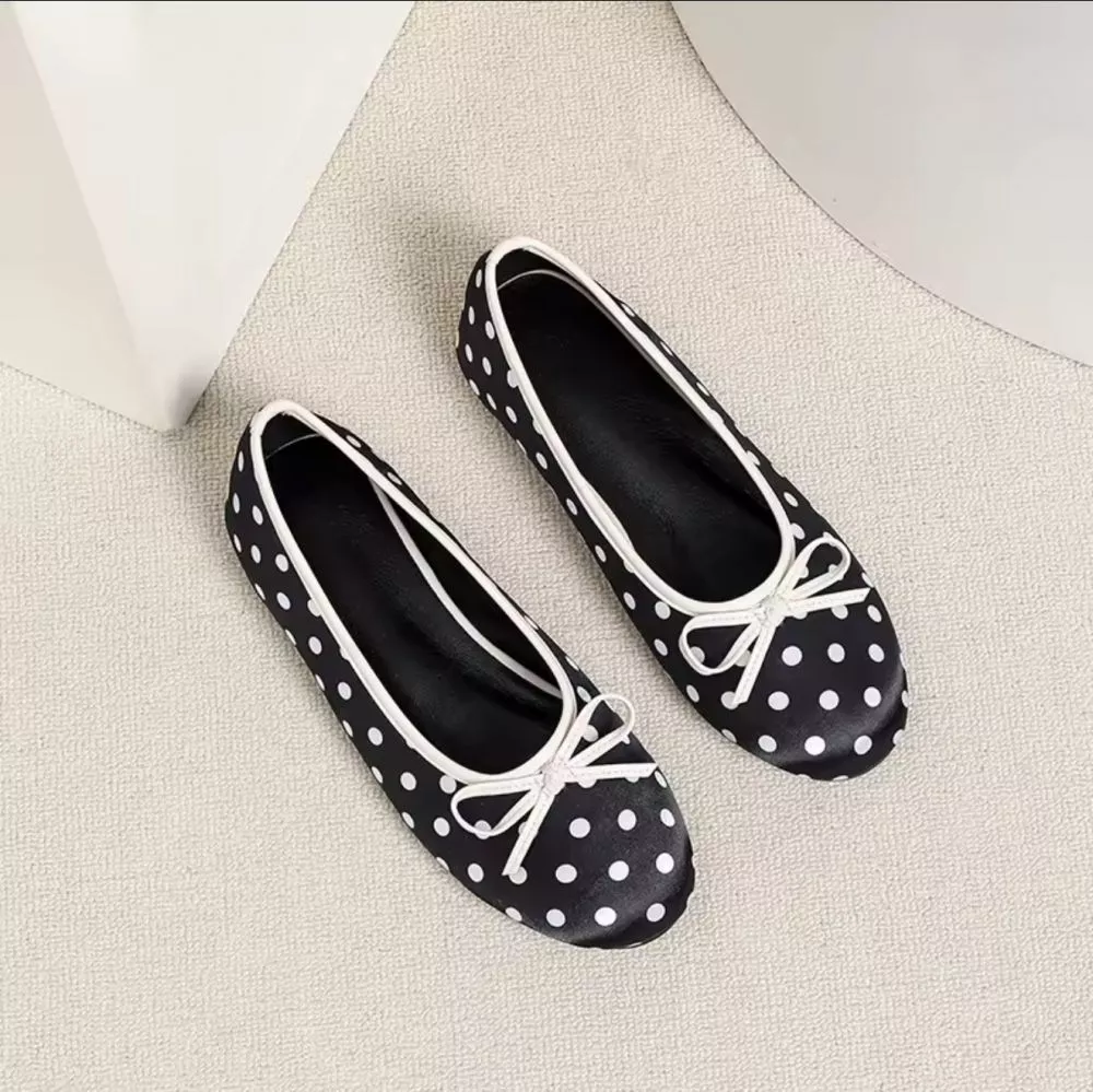 Ballerine donna nero con pois bianchi e fiocco, viste dall'alto, su pavimento chiaro.