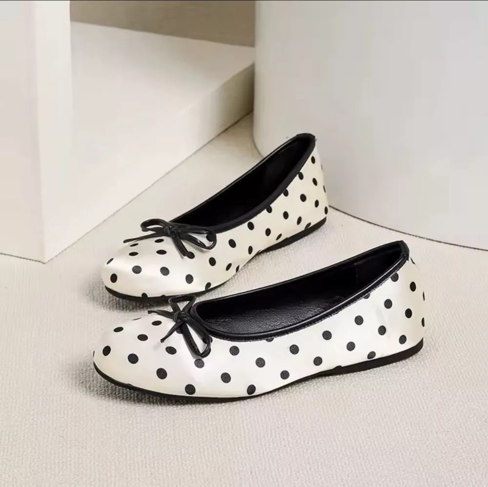 Ballerine donna bianco con pois neri e fiocco, viste lateralmente, su pavimento chiaro.