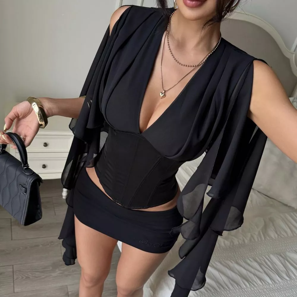 Donna che indossa blusa nera elegante con corsetto e maniche volant essendo accovacciata
