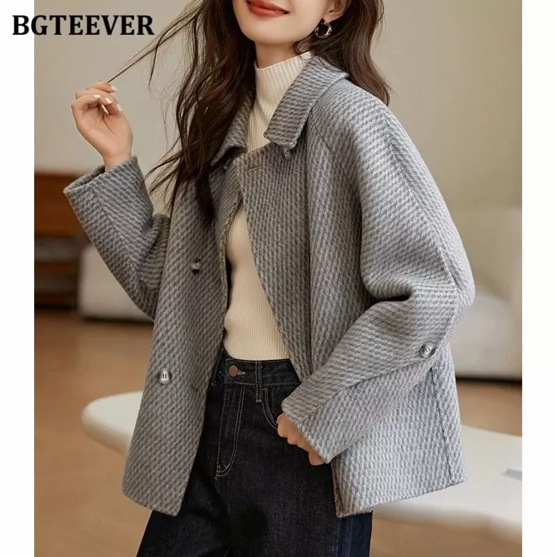 Modella indossa cappotto donna grigio doppiopetto con maglione a collo alto bianco e jeans neri