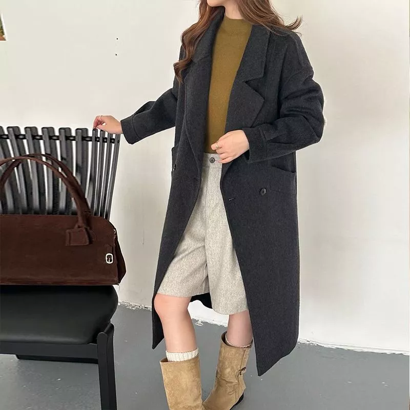 Donna con cappotto nero lungo posa con borsa marrone e stivali beige
