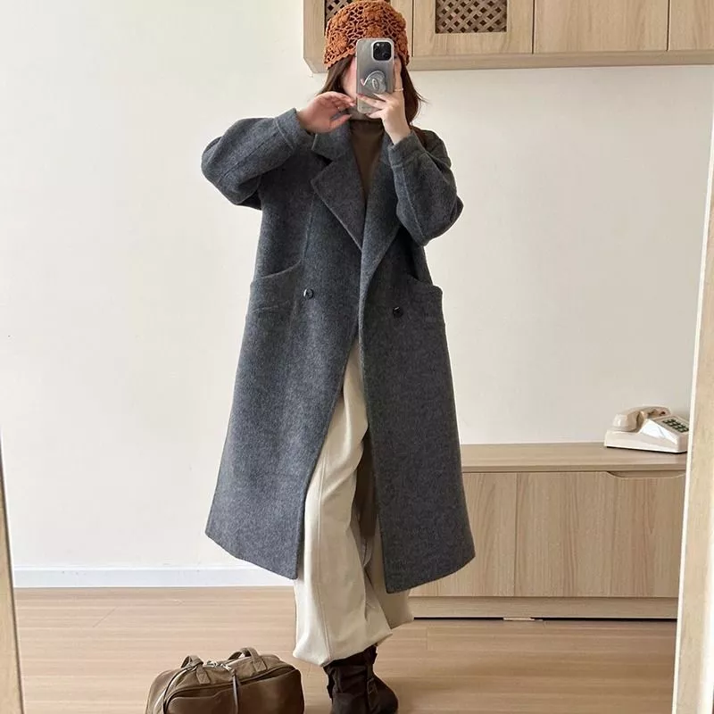 Donna con cappotto grigio lungo e pantaloni beige davanti a mobile basso