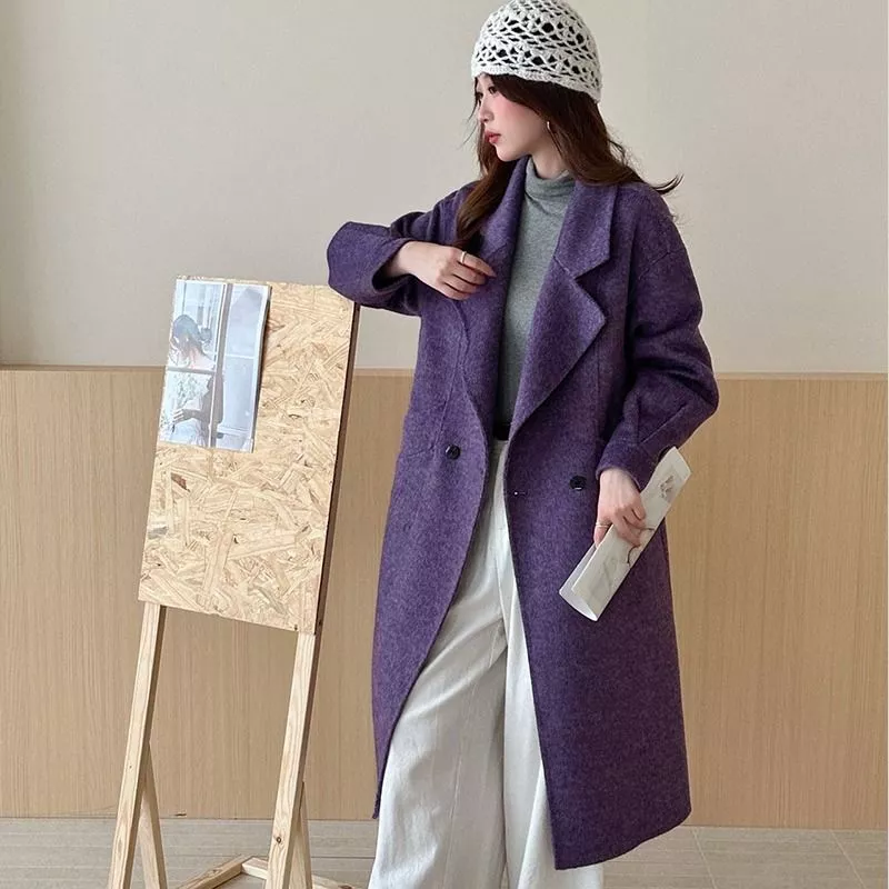 Donna con cappotto viola lungo e berretto bianco, tiene in mano rivista