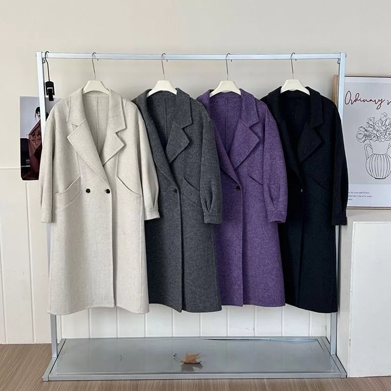 Donna con cappotto nero lungo, maglia verde oliva e borsa marrone in interno