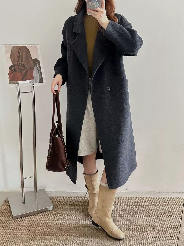 Donna con cappotto nero lungo e berretto bianco fotografata davanti a parete