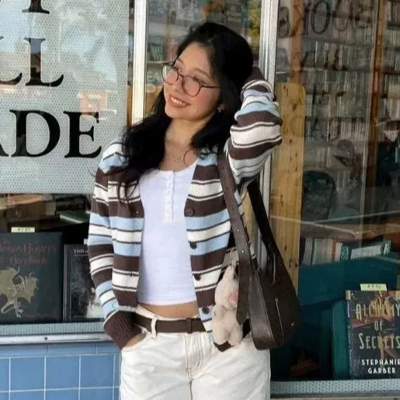 Donna con cardigan a righe marrone azzurro bianco e top bianco sorride davanti a libreria