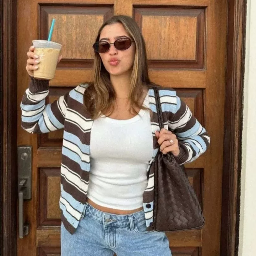 Donna con cardigan rigato marrone azzurro e bianco al sole davanti ad edificio