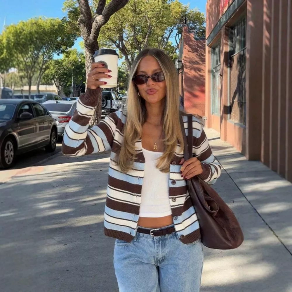 Donna con cardigan a righe marrone azzurro bianco e jeans posa sorridente all'aperto