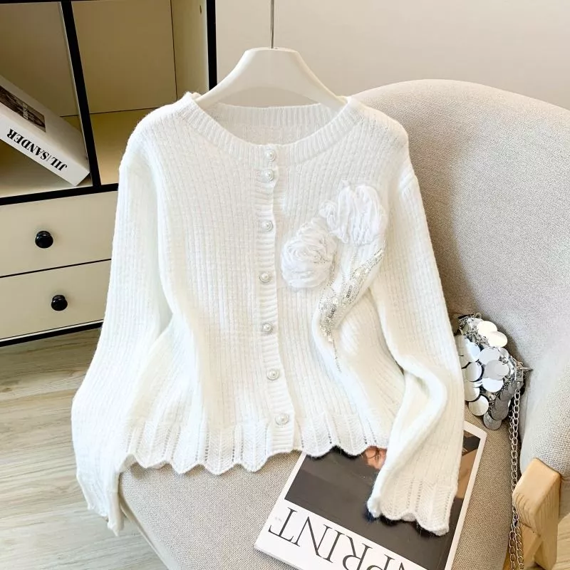Cardigan donna bianco in maglia con decorazione floreale, appoggiato su sedia