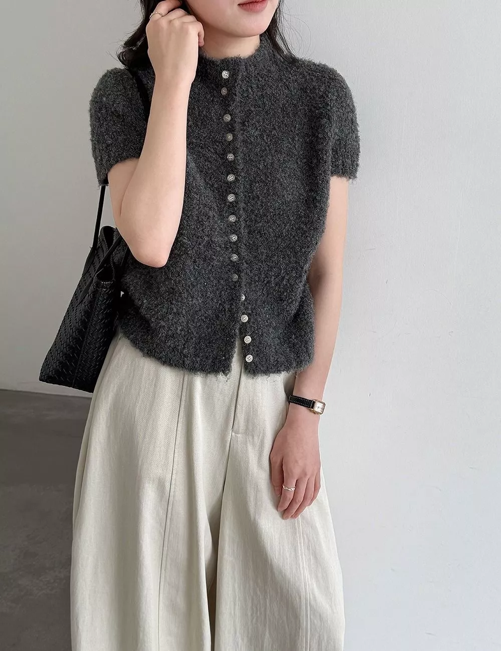 Modello indossa cardigan grigio con maniche corte, pantaloni chiari larghi e borsa nera