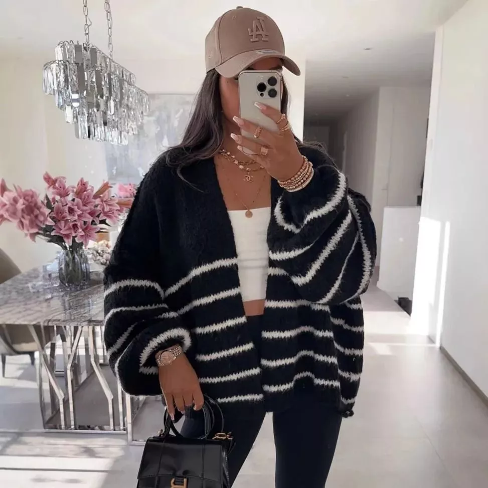 Cardigan nero con righe bianche tenuto aperto con borsa nera