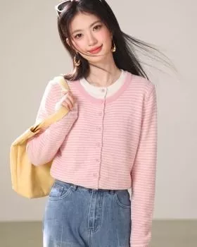 Modella con cardigan rosa a righe chiuso che sorride con borsa gialla e jeans chiari