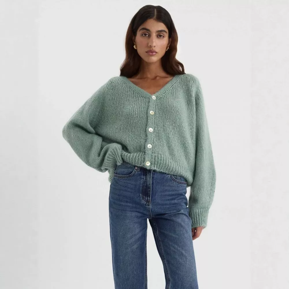 Modella indossa cardigan bianco con scollo a V e bottoni, vista laterale.