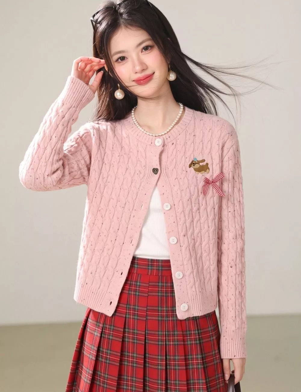 Modello che indossa il cardigan rosa con maniche lunghe, abbinato a top bianco e gonna plissettata rossa