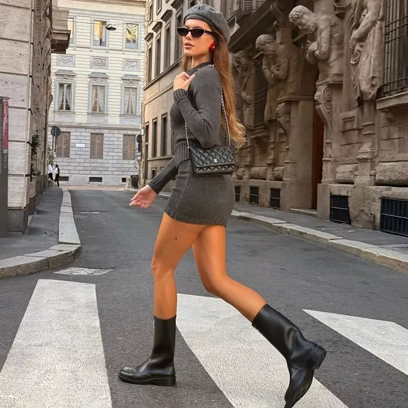 Donna che cammina con completo maglia e gonna grigio scuro e stivali neri