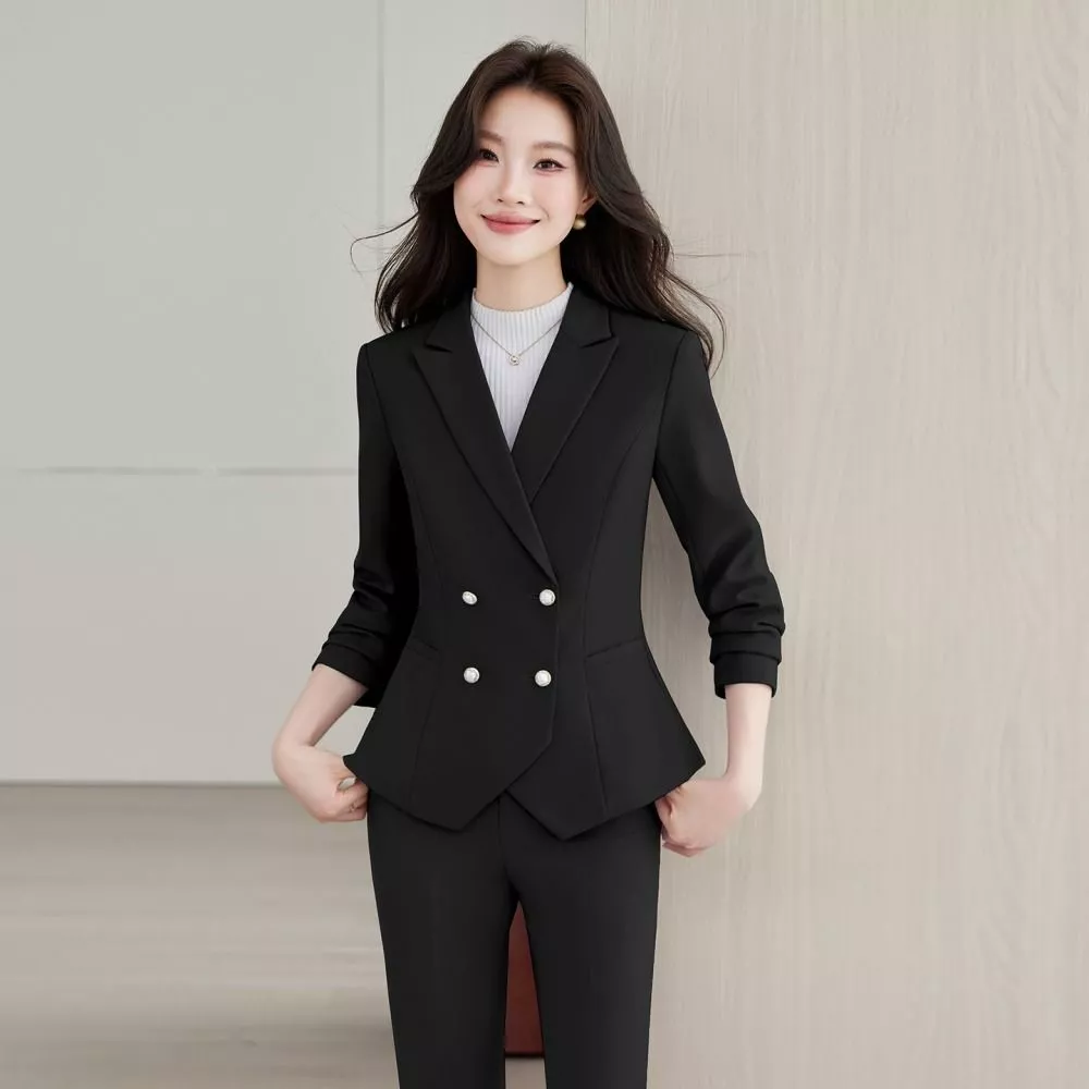 Donna in completo nero con giacca doppiopetto decorata con bottoni gioiello e pantaloni abbinati, sorridente con mani sulle tasche