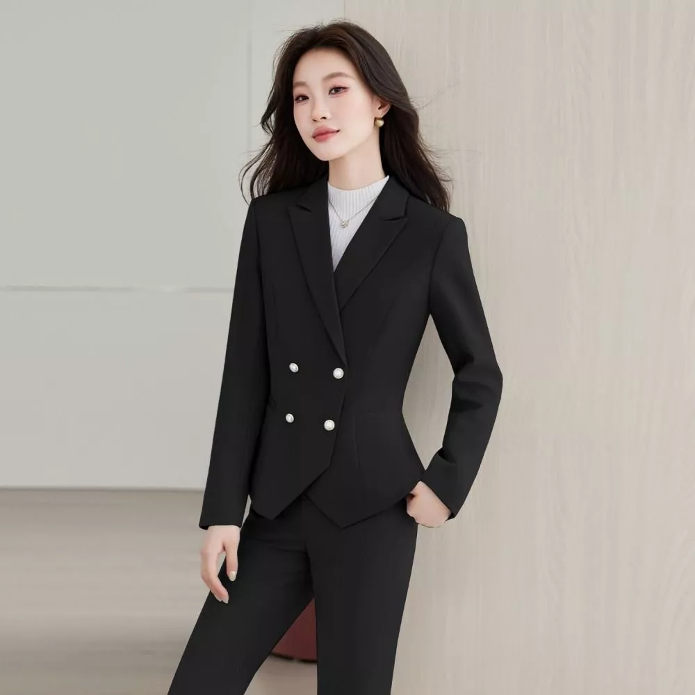 Donna in completo beige con giacca doppiopetto e pantaloni classici, mani davanti