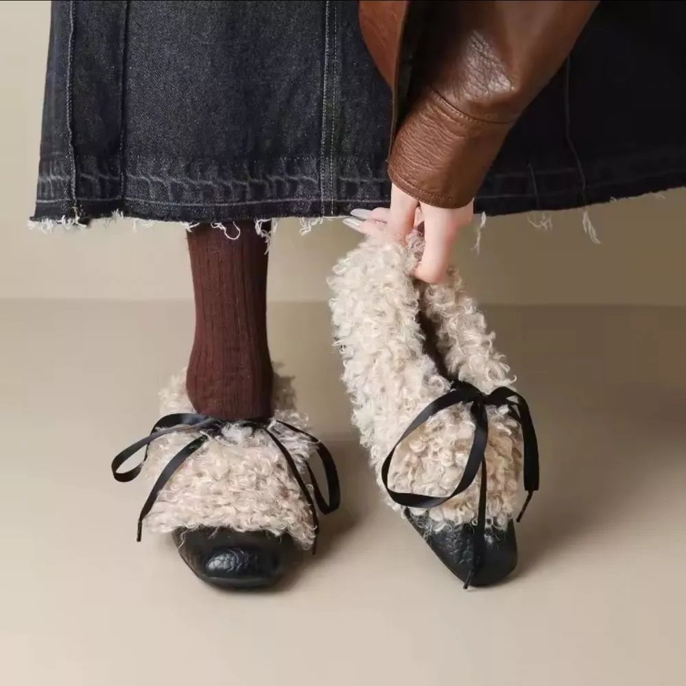 Dettaglio d&eacute;collet&eacute; nere in pelo sintetico con fiocco nero, viste frontali con mano che tiene una scarpa e calze marroni.