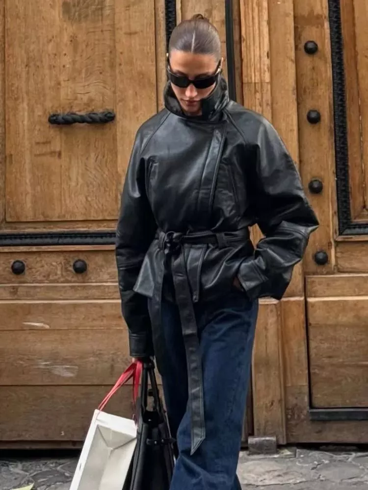Modella indossa giacca in pelle sintetica nera con cintura annodata e shorts