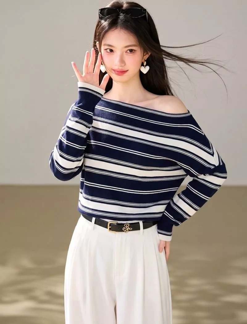Modello sorride indossando maglione blu rigato con scollo ampio