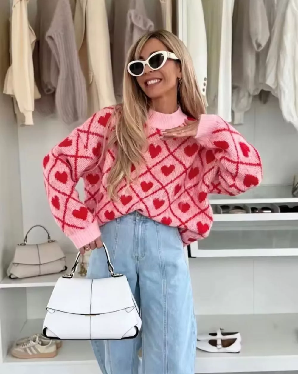 Maglione donna rosa con cuori rossi indossato frontalmente con braccio piegato e jeans chiari