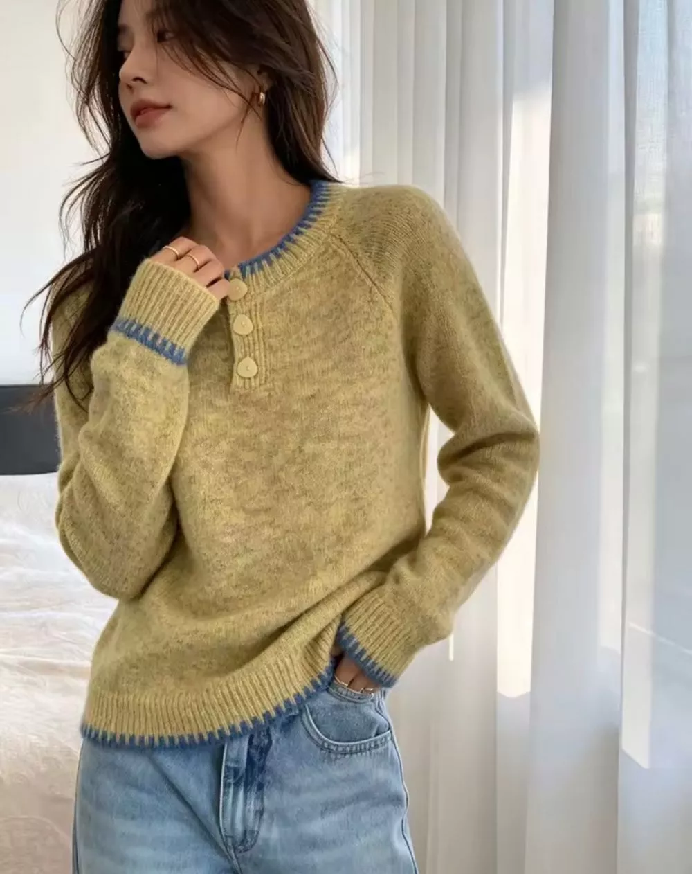 Modella indossa maglione verde con dettagli blu e bottoni sul davanti in ambiente interno con tende bianche