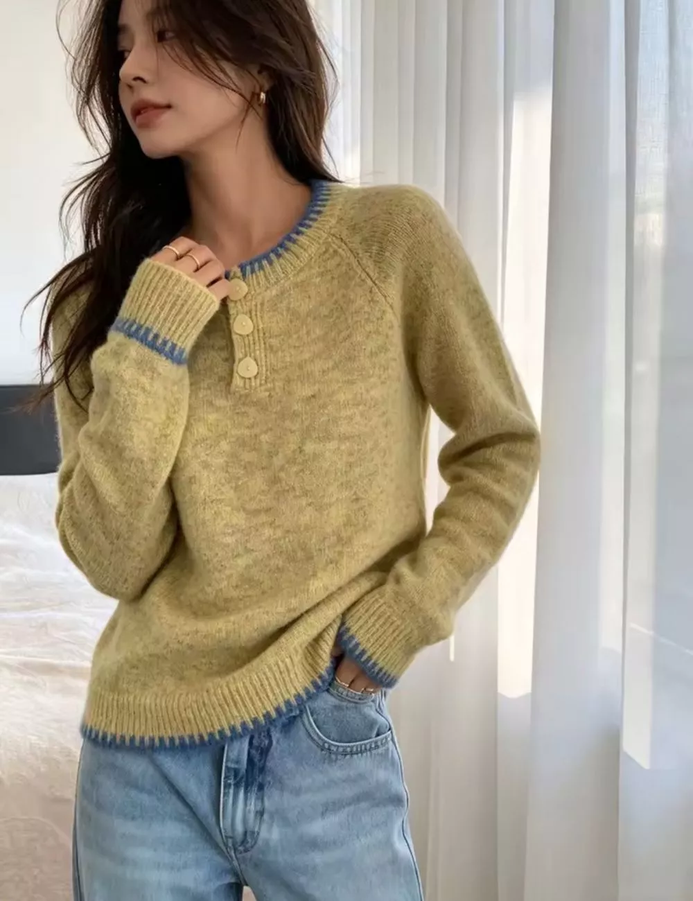 Dettaglio manica maglione verde con bordo blu, modella che tiene la mano vicino al viso