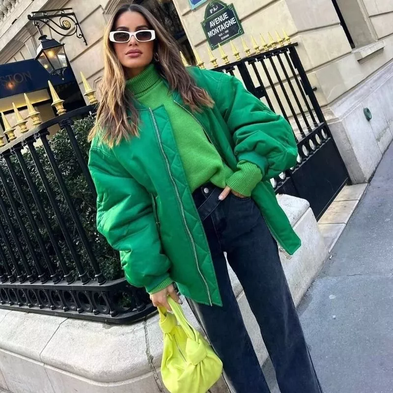 Donna con piumino verde oversize, abbinato a maglione verde e borsa gialla
