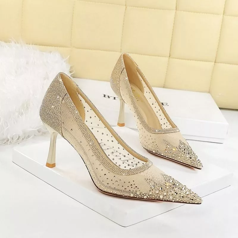 Dettaglio laterale delle scarpe oro con tacco sottile e fascia superiore in tessuto glitterato.