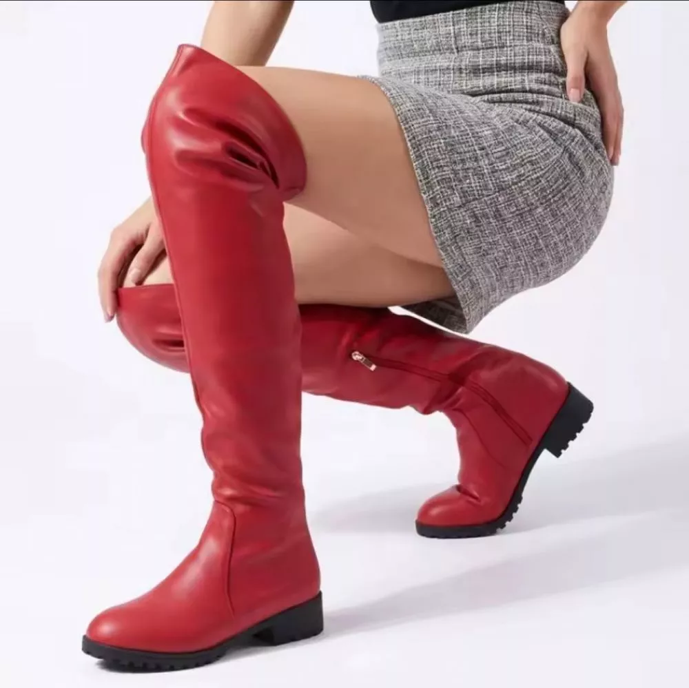 Stivali sopra il ginocchio rossi in materiale sintetico indossati da donna con minigonna grigia a quadri.