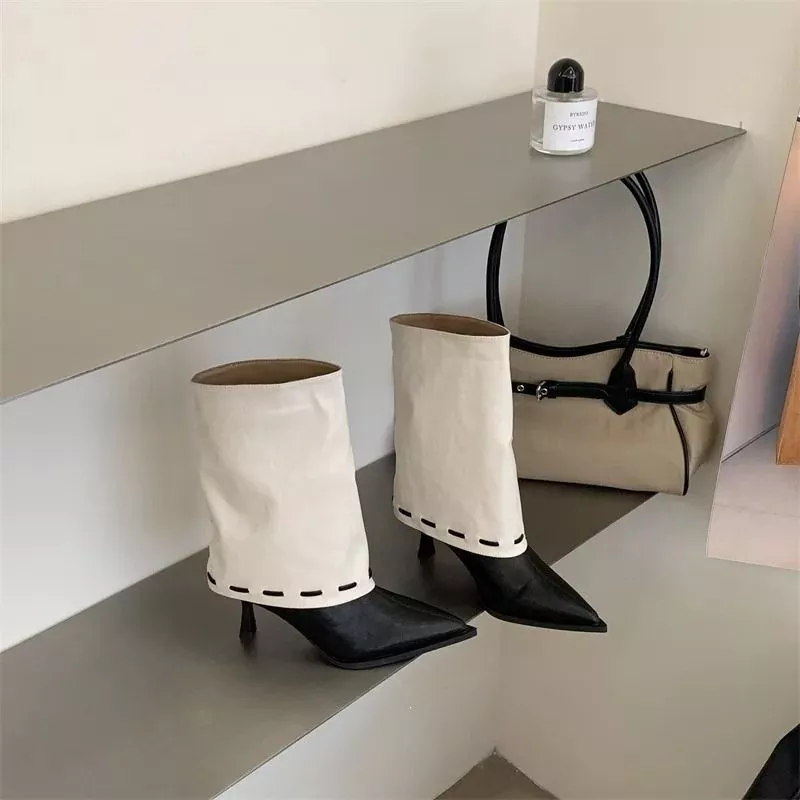 Modella con tronchetti beige e punta nera, dettaglio gambale in materiale sintetico scamosciato