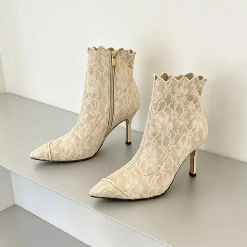 Tronchetti beige in pizzo con tacco alto e zip laterale su superficie grigia