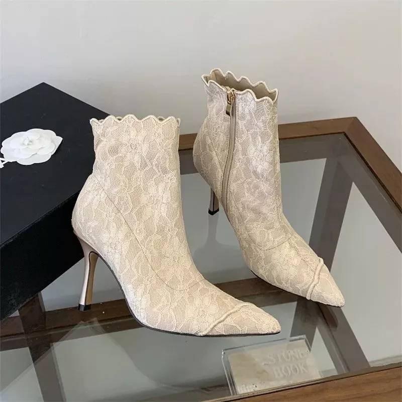 Tronchetti beige in pizzo con tacco alto su tavolo di vetro accanto a scatola nera